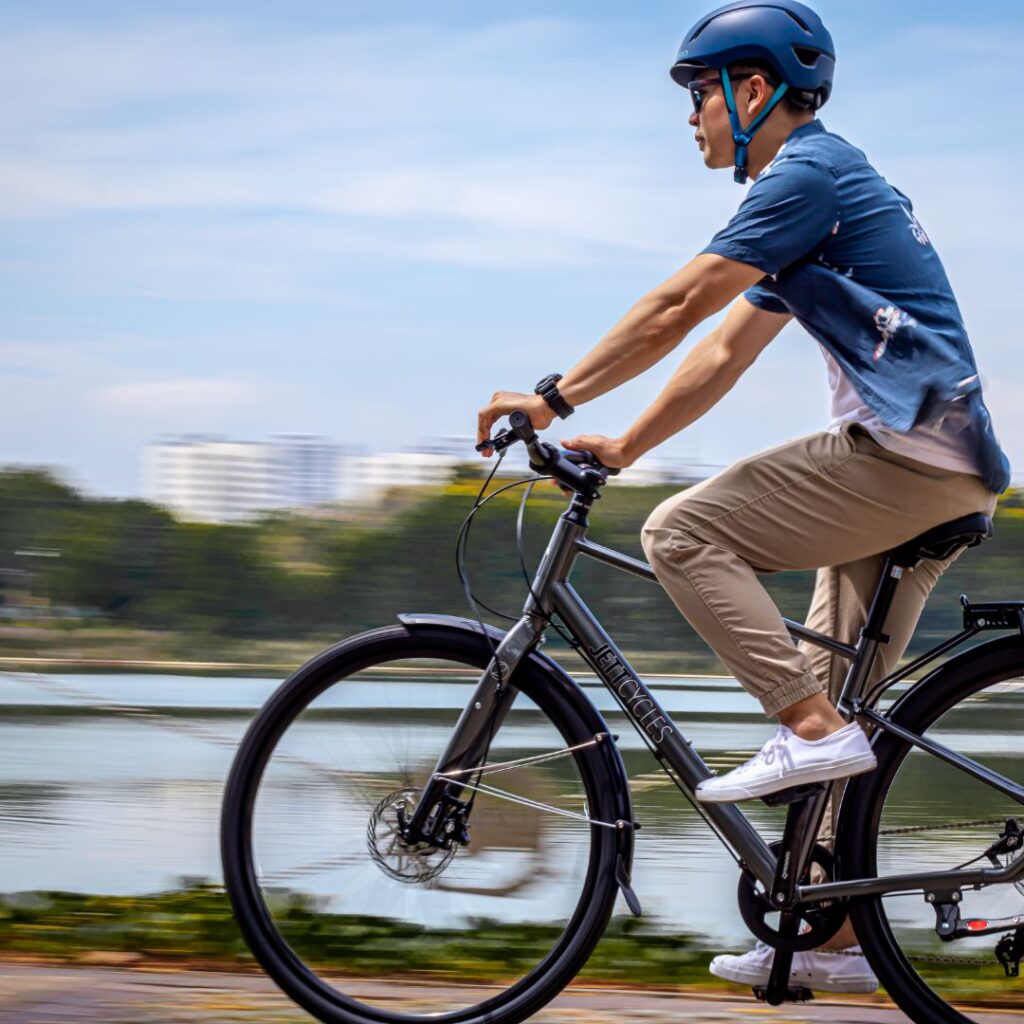 A man wearing a helmet and sunglasses riding a e-bicycle along a waterfront path.