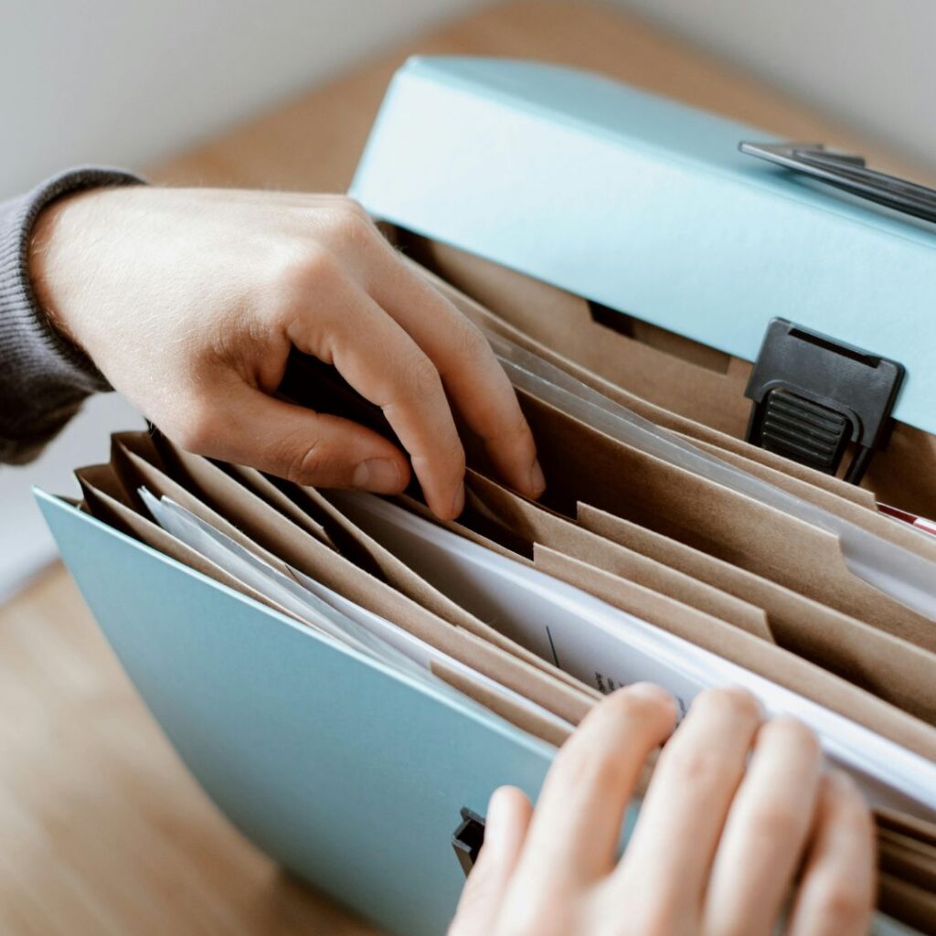 Close-up of hands reaching into a light blue expanding file folder with multiple dividers to sort papers.