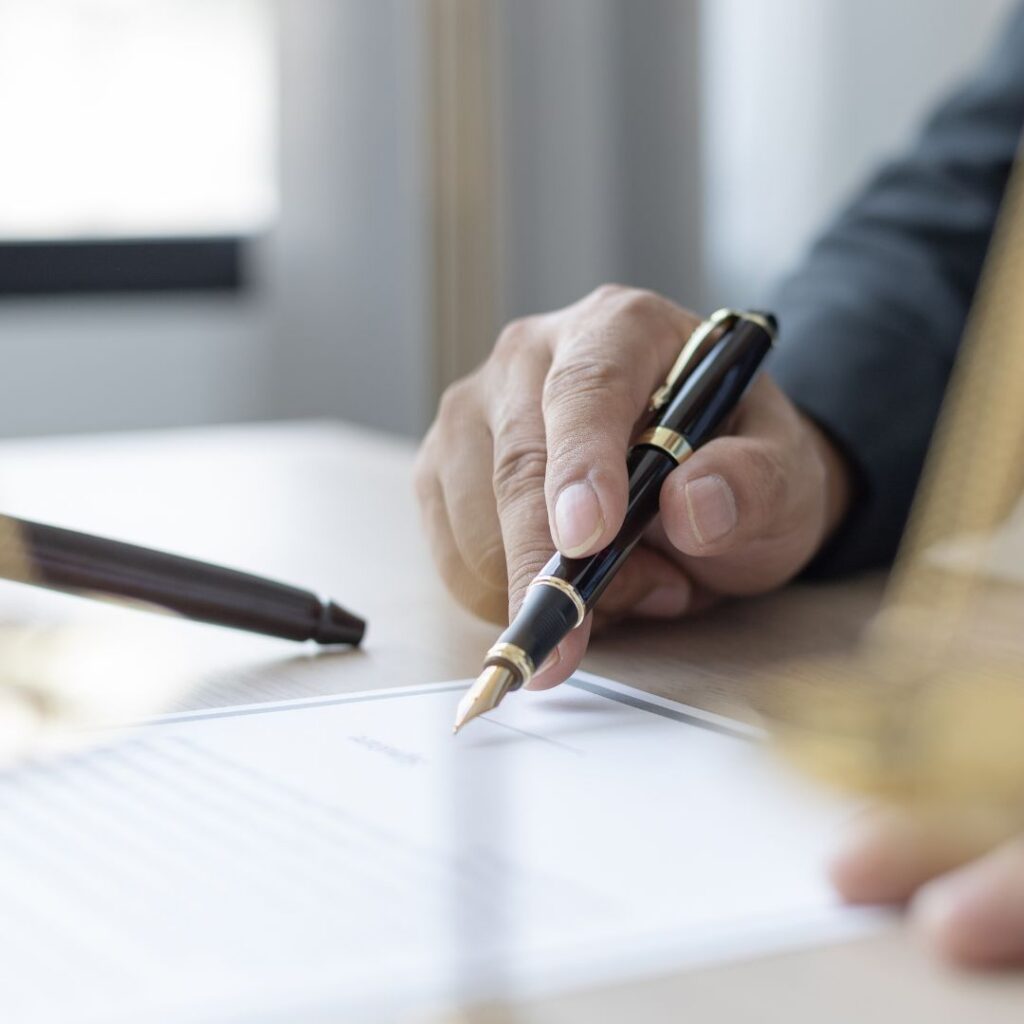 Close-up of a hand signing a legal document on a desk using a fountain pen.